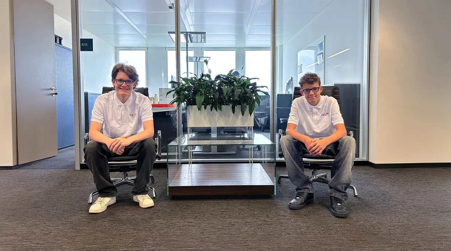 Lernende Thierry und Tom sitzen auf Stühlen im Büro
